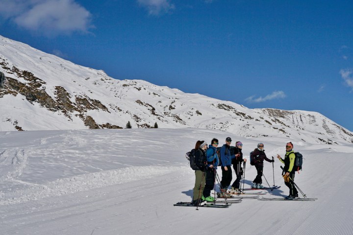 Group of skiers on a snowy mountain slope under a clear blue sky.