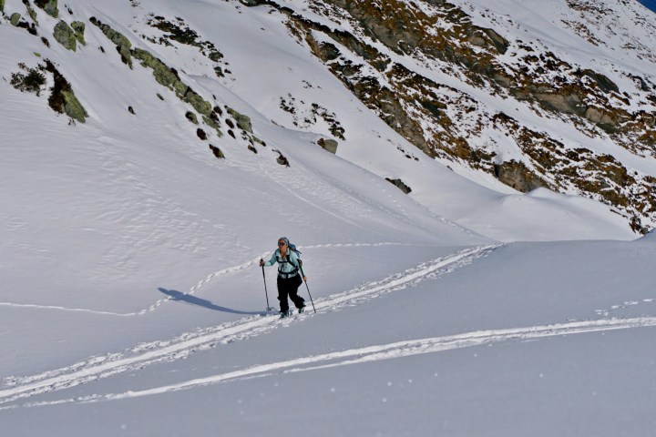Person skiing uphill on a snowy mountain slope with ski poles.