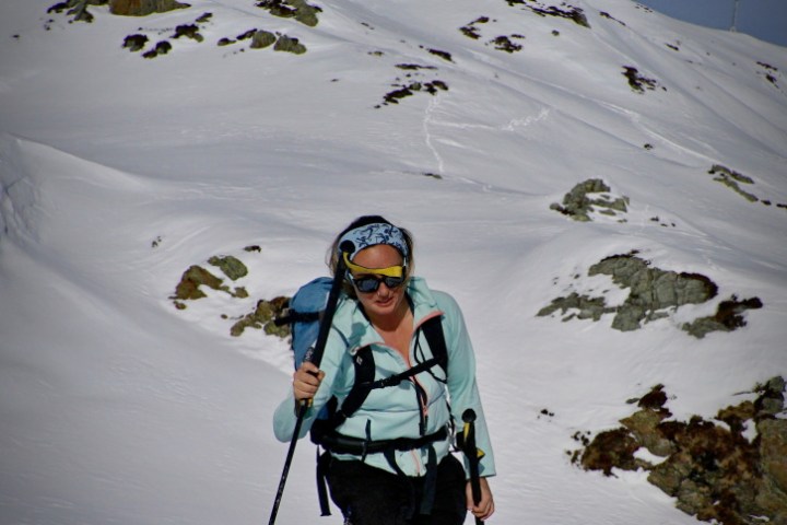 Person snowshoeing up a snowy mountain slope with ski poles under a clear blue sky.