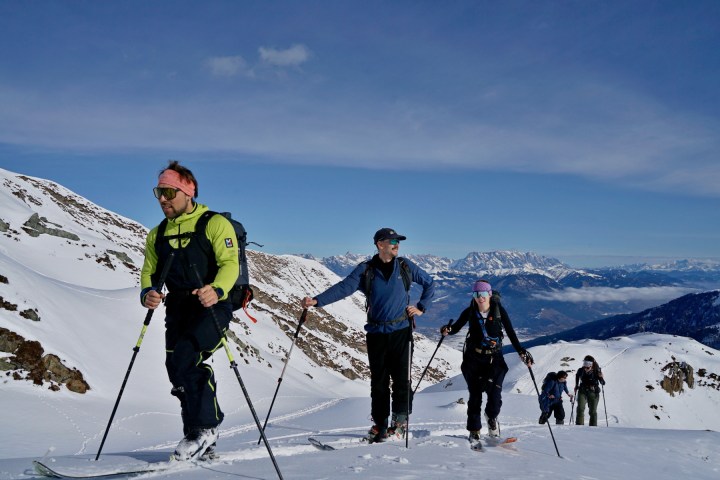Group of people skiing uphill on a snowy mountain with a clear blue sky.