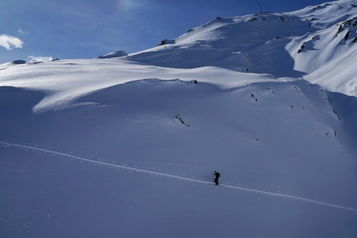Person walking on a snowy mountain slope under a clear blue sky.