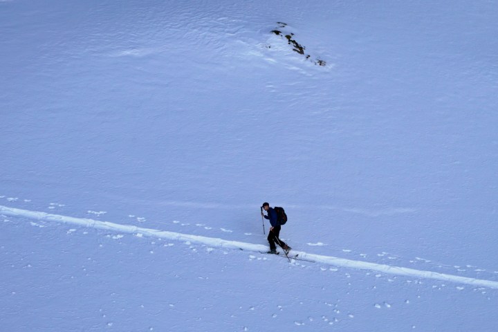 Person skiing uphill on a snowy slope with a backpack and poles.