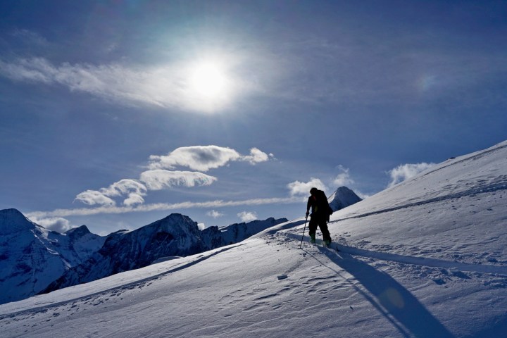 Person hiking uphill in snowy mountains under bright sun and blue sky.