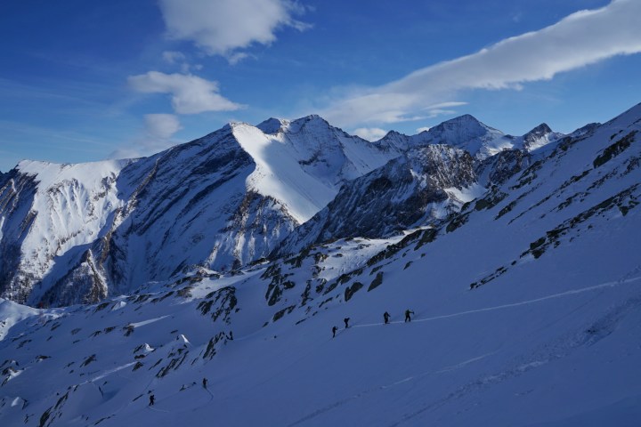 Hikers ascending a snow-covered mountain with a scenic view of snowy peaks and blue sky.