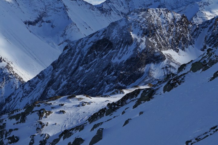 Four climbers ascend a snowy mountain slope with jagged peaks in the background.