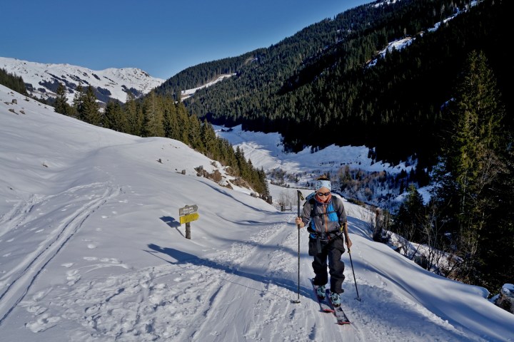 Person skiing uphill on a snowy mountain trail surrounded by trees.