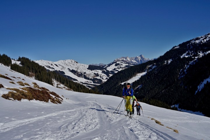 Two skiers ascending a snowy mountain trail with a scenic view in the background.