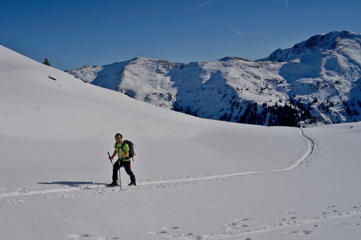 Person skiing uphill on snowy mountain with clear blue sky.