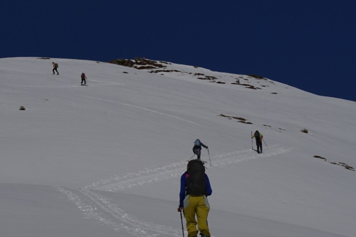 Skiers ascending a snow-covered slope under a clear blue sky.