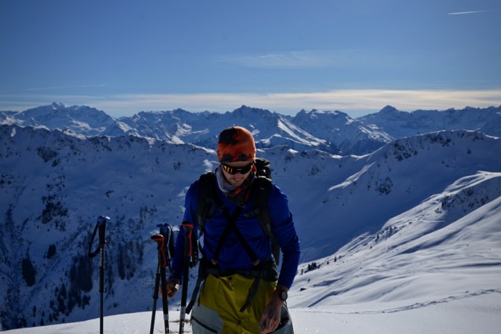 Person skiing on snowy mountain with ski poles under bright sun.