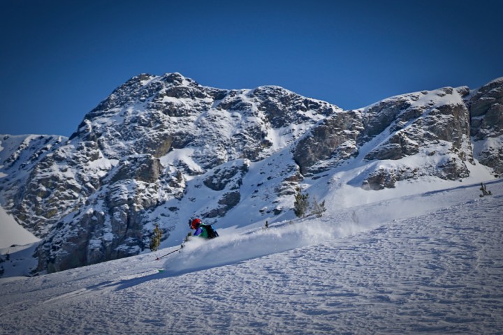 Skier in red helmet skiing on snowy mountain slope with rocky peaks in background.