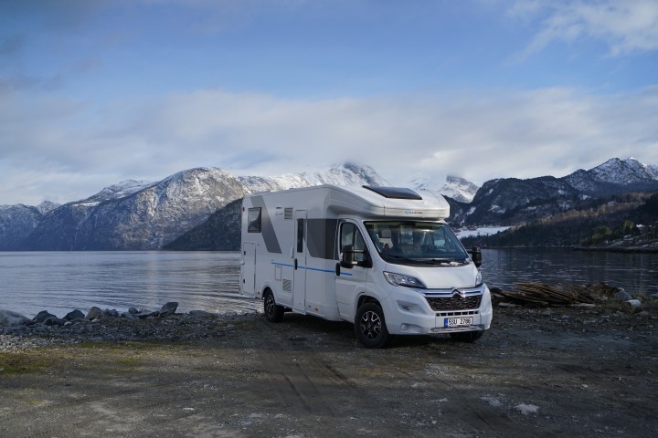 Camper van parked by a calm lake with snow-capped mountains in the background.