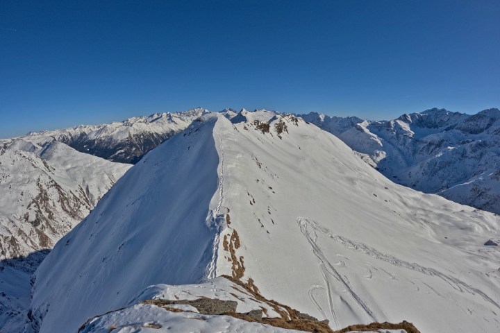 Snow-covered mountain ridge under clear blue sky with distant peaks.