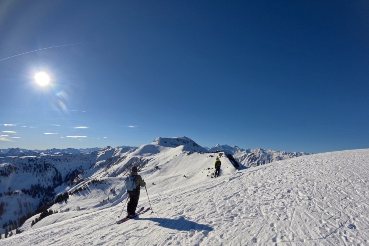 Two skiers on snowy mountain slope under bright sun and clear blue sky.