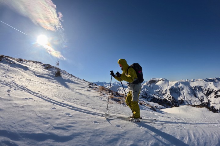 Skier in yellow gear climbing a snowy mountain under a bright sun with a clear blue sky.