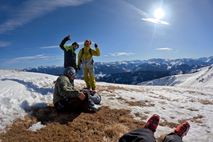 Three people in winter gear on a snowy mountain with a sunny sky.