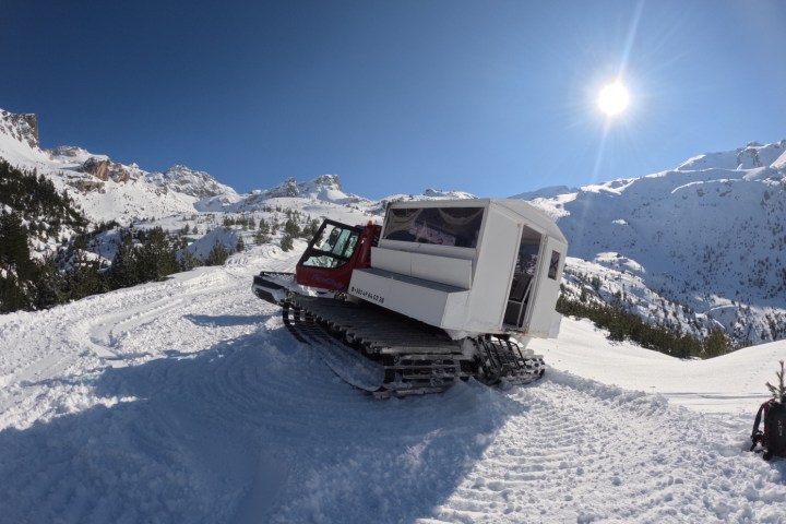 Snowcat with cabin on snowy mountain under bright sun and blue sky.