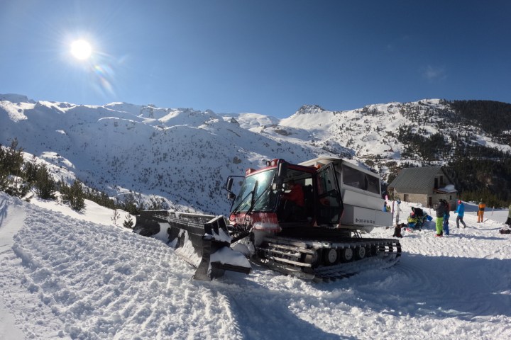 Snowplow on snowy mountain slope under clear blue sky, skiers nearby.