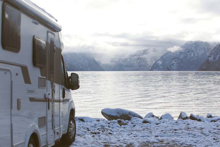 Campervan parked by a snowy lake with mountains in the background.