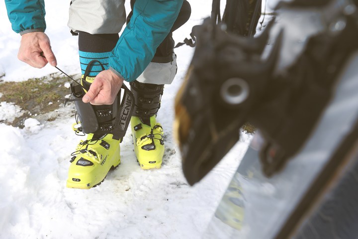 Person in ski gear adjusting bright yellow ski boots on snowy ground.