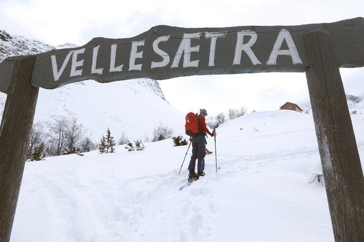Person skiing uphill in snow under Vellesætra sign with mountain background.