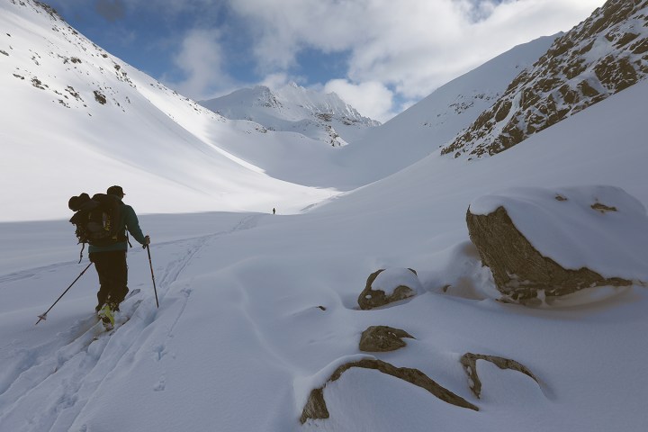 Person skiing uphill in a snow-covered mountain landscape under a blue sky.