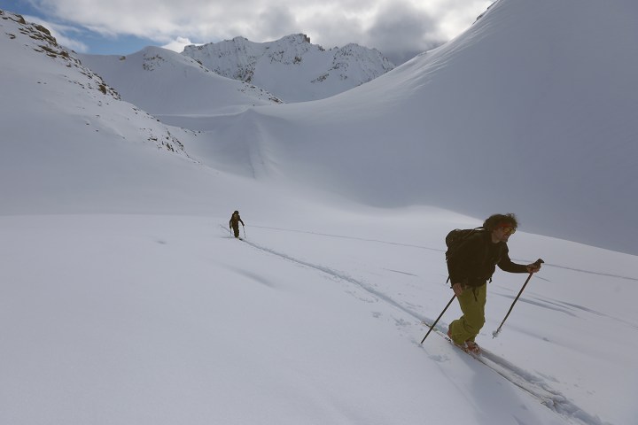 Two people skiing uphill on a snowy mountain with clear skies.