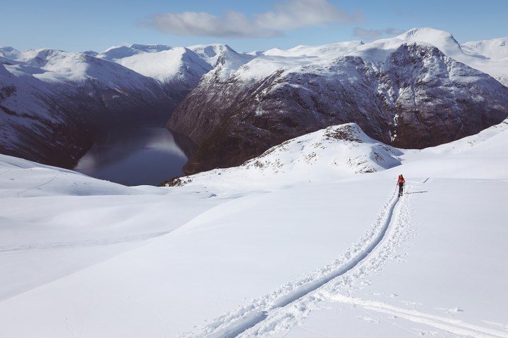 Person skiing uphill on snow-covered mountain with fjord view.