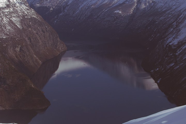 Snowy mountains and a calm fjord under a clear blue sky.