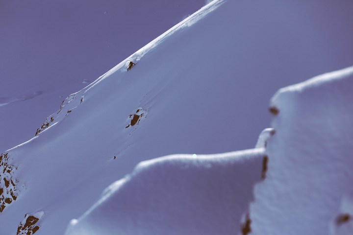 A snowy mountain ridge with visible rocks on a clear day.