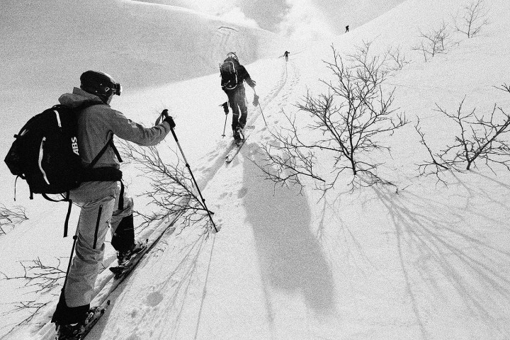 Skiers ascending a snowy slope with trees and shadows in a black and white scene.
