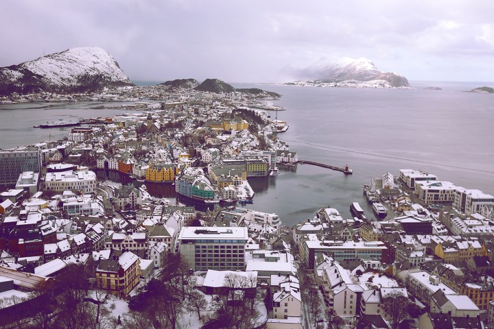 Aerial view of a snowy coastal city with colorful buildings and mountains in the background.