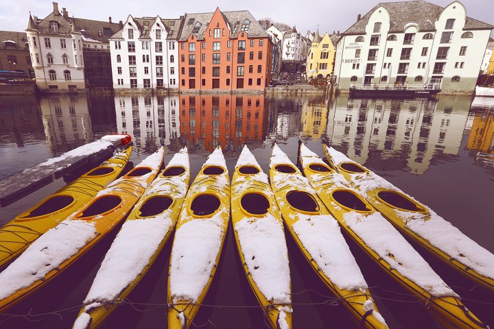 Snow-covered yellow kayaks on water with colorful buildings reflected in background.