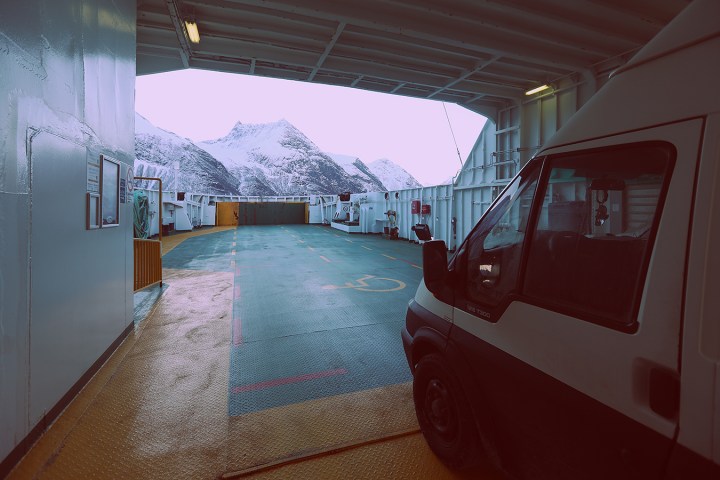 Van parked on ferry deck, snowy mountains visible through open door.