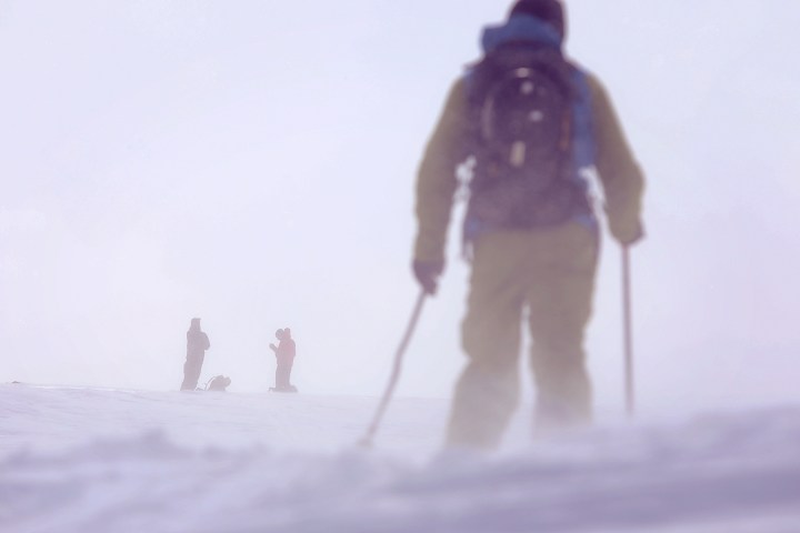 People skiing in foggy, snowy conditions with poor visibility on a mountain.