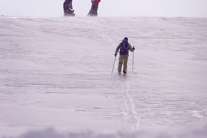 Three skiers ascend a snowy hill under a cloudy sky.