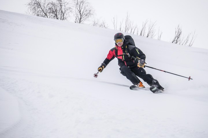 Skier in red and black gear carving through snow on a steep slope.
