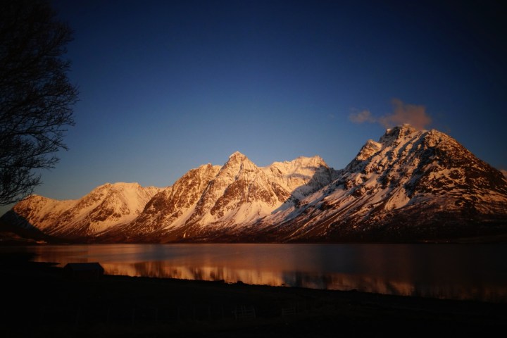 Snowy mountains reflected in a calm lake at sunset.