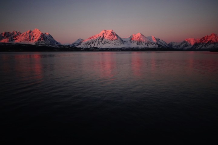 Snowy mountains at sunset with pink reflections on a calm lake.