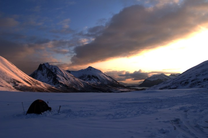 Snowy mountains at sunset with a tent in the foreground.