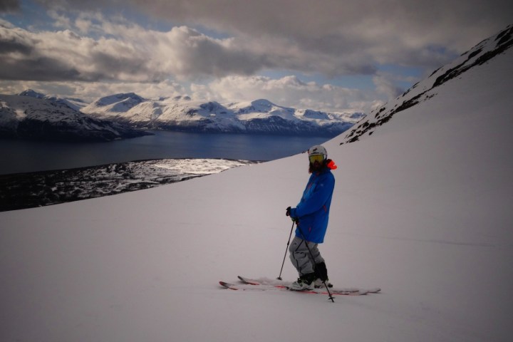 Person skiing on snowy mountain with scenic view of fjord and mountains in the background.