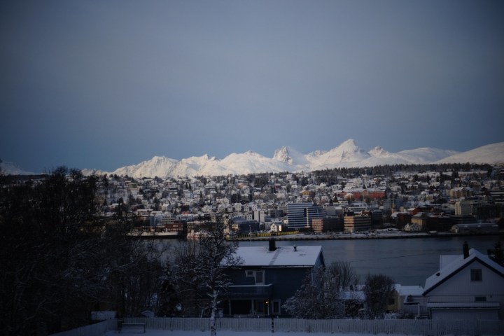 Snow-covered mountains behind a cityscape with snowy rooftops and dark sky.