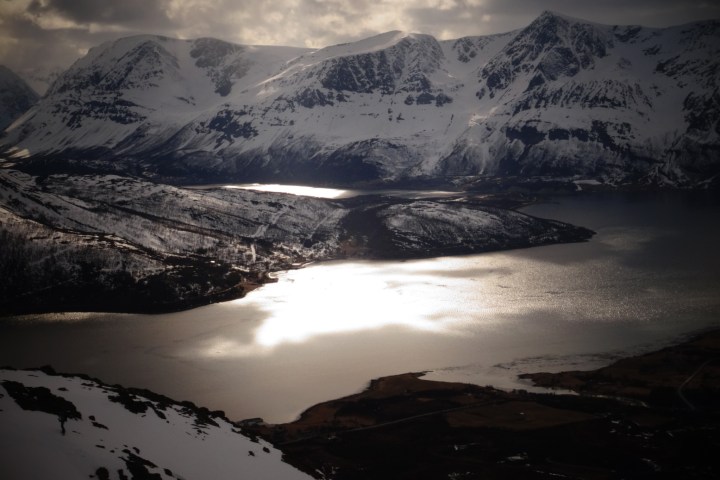 Snowy mountains and reflective lake under cloudy sky at sunset.
