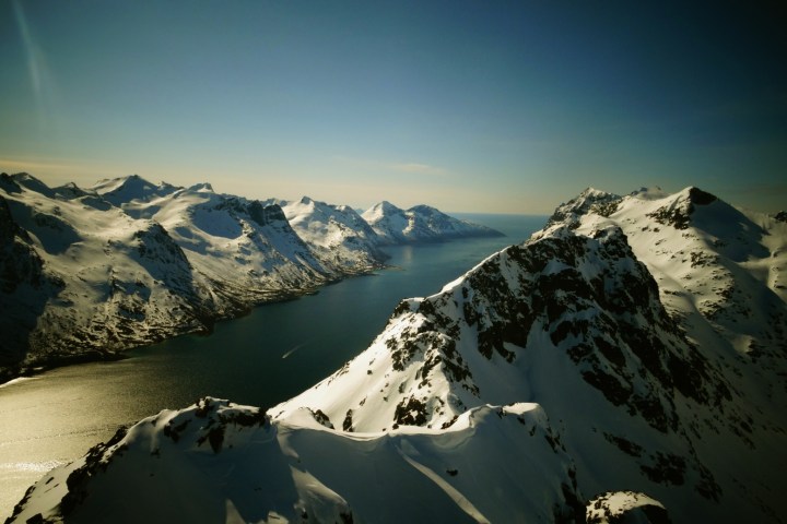 Snowy mountain peaks and a fjord under clear blue sky.