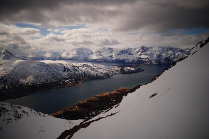 Snowy mountain landscape with a lake under a cloudy sky.