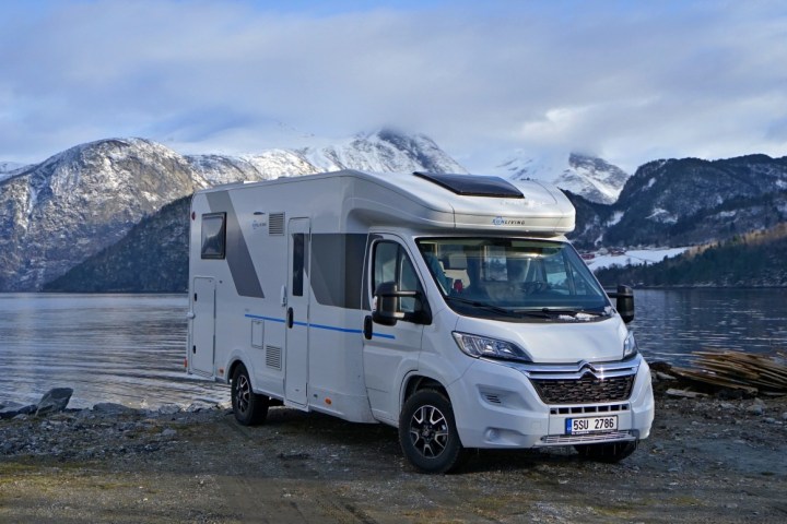 White camper van parked by a lake with snowy mountains in the background.