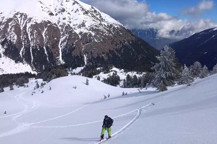 Skier in bright pants ascends snow-covered slope with mountain backdrop.