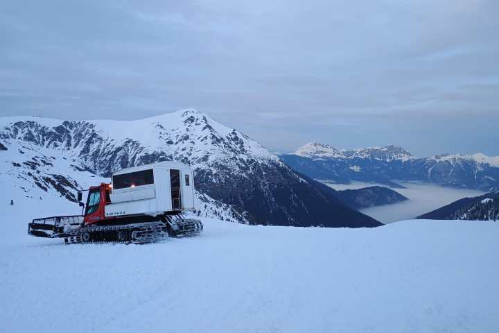 Snowcat on a snowy mountain with distant foggy valleys and peaks.