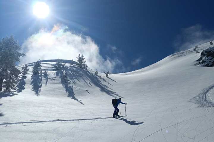 Person skiing uphill on a sunny snow-covered mountain slope under a clear blue sky.