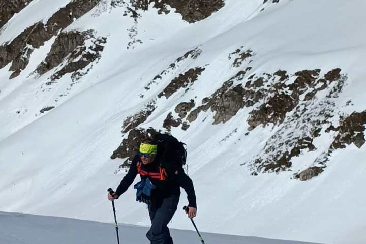 Skier climbing snowy mountain with poles, mountains in the background.